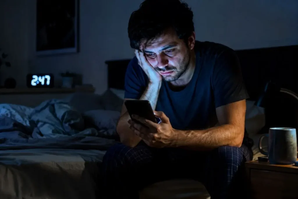 Homem com aparência cansada sentado na cama durante a madrugada após dormir pouco