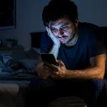 Homem com aparência cansada sentado na cama durante a madrugada após dormir pouco